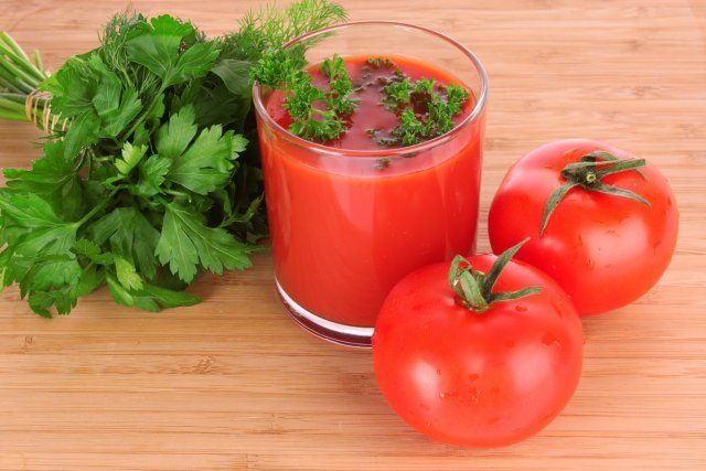 Glass of fresh tomato juice and tomatoes round the glass on the table