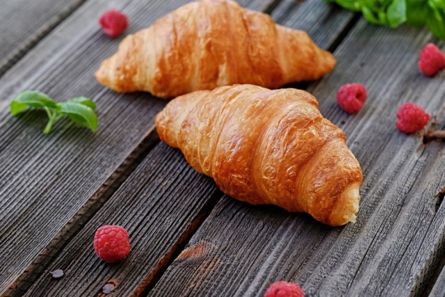 Two fresh croissants on a wooden table.