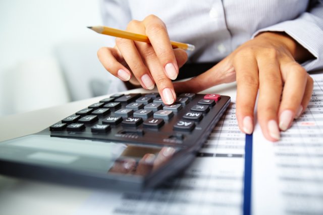 Photo of hands holding pencil and pressing calculator buttons over documents 